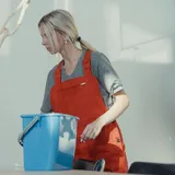 Uploaded photo, square: a cleaner in red overalls wringing a cloth over a blue bucket.